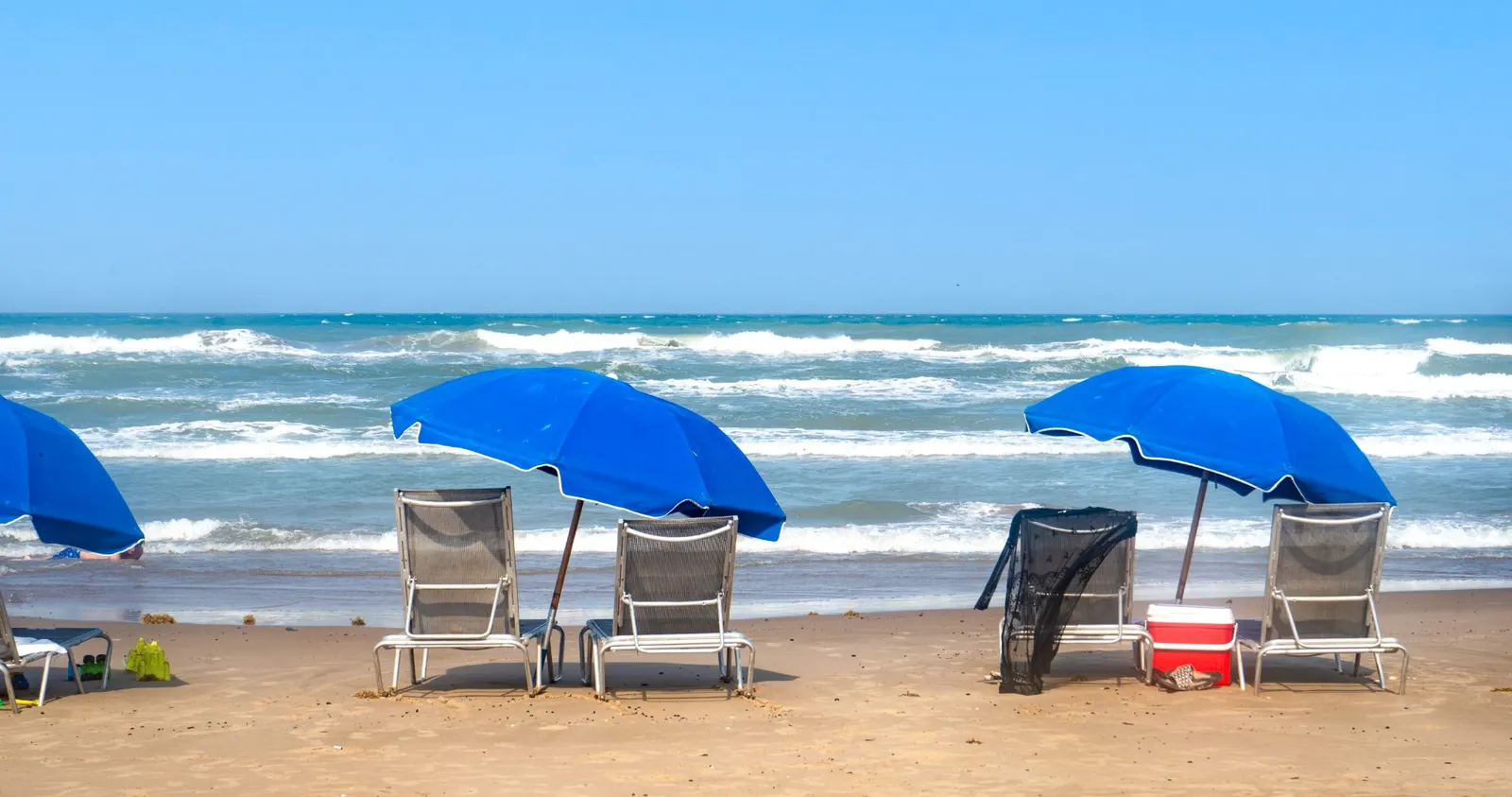 Blue umbrellas and lounge chairs set up on the sand, facing the waves