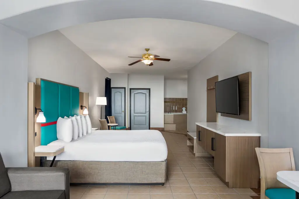 King bed with a teal headboard, a wall TV and a kitchenette counter