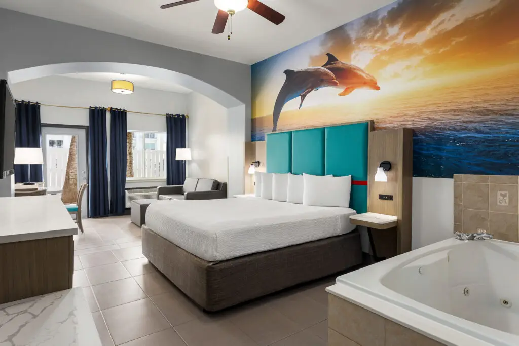 King bed under a dolphin mural, with a jetted tub in the foreground