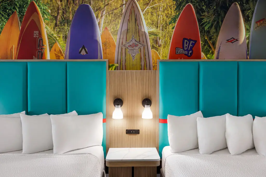 Dos camas queen con cabeceras turquesa bajo un mural de tablas de surf