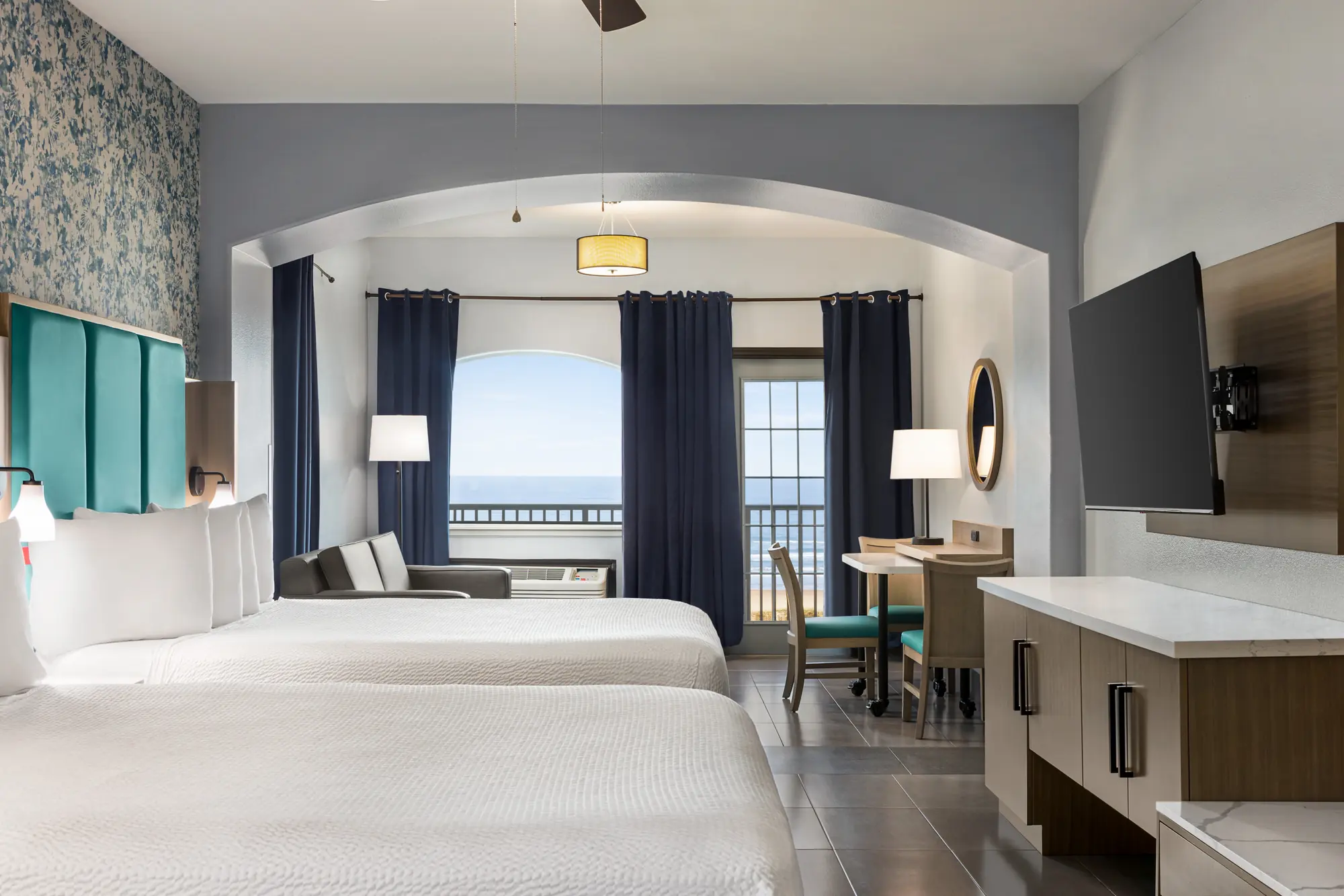 Two queen beds, blue floral wallpaper and balcony doors open to the ocean