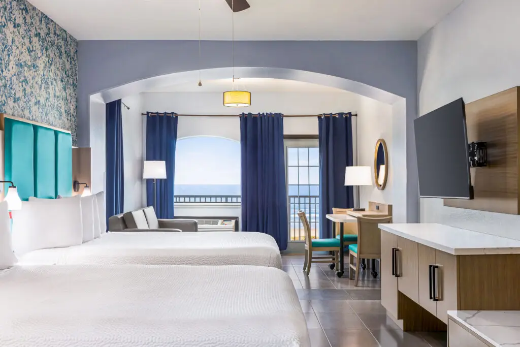 Two queen beds, blue floral wallpaper and balcony doors open to the ocean