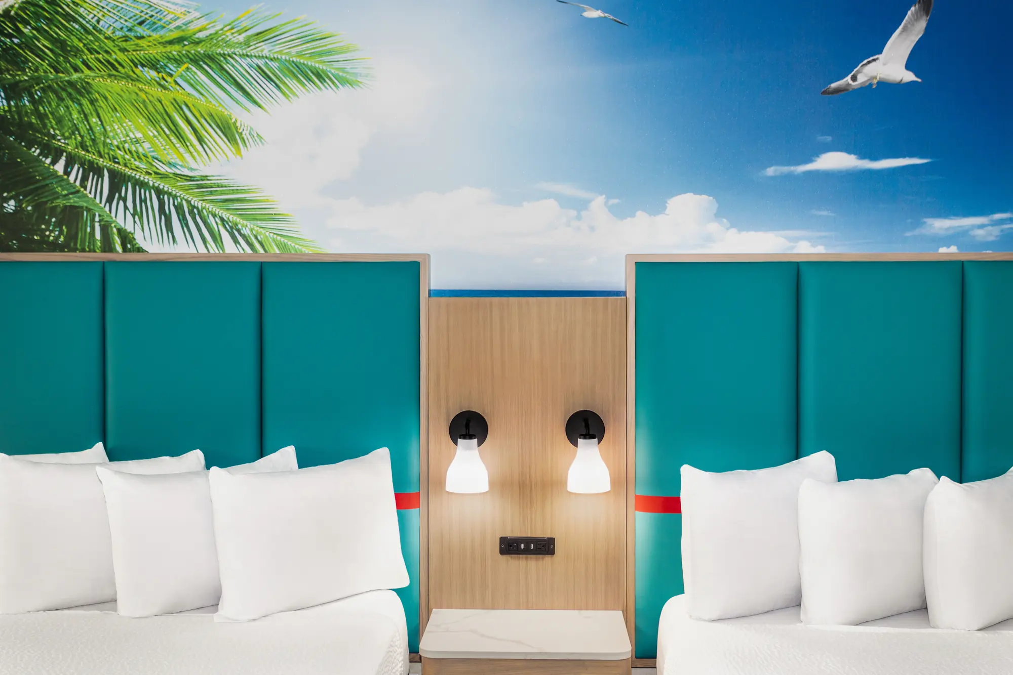 Two beds with teal headboards under a palm tree mural