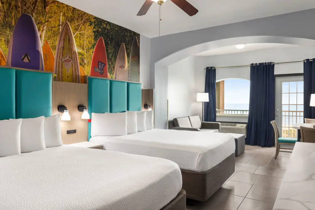 Habitación con dos camas queen, cabeceras turquesa y un mural de tablas de surf